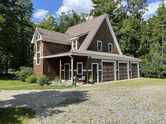 view of front facade with a chimney, a shingled roof, covered porch, a garage, and driveway