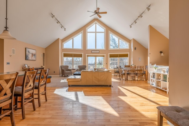 living room with ceiling fan, rail lighting, high vaulted ceiling, and light wood-type flooring