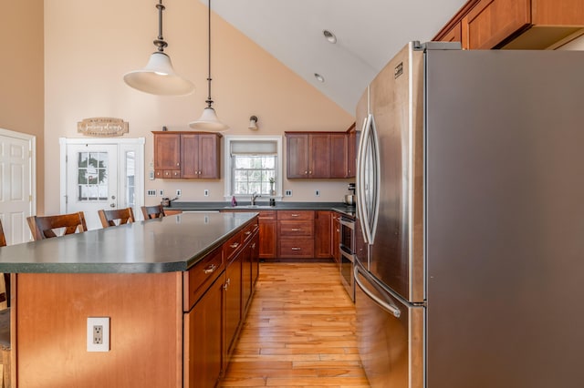 kitchen with sink, decorative light fixtures, appliances with stainless steel finishes, a kitchen island, and light hardwood / wood-style floors