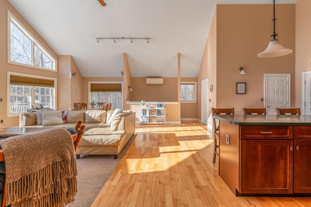 living room with a wall mounted air conditioner, light hardwood / wood-style flooring, high vaulted ceiling, and track lighting