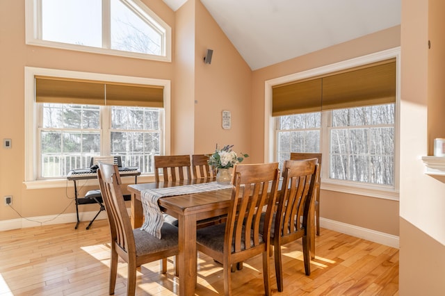 dining area with high vaulted ceiling and light hardwood / wood-style floors