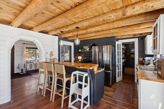 kitchen with butcher block counters, sink, beamed ceiling, stainless steel fridge, and pendant lighting