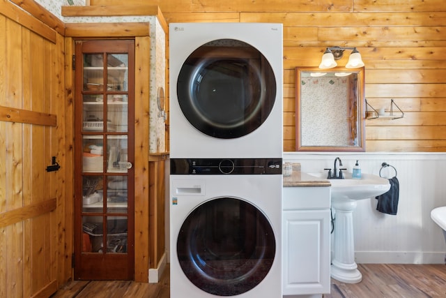 laundry area featuring stacked washer and clothes dryer, wooden walls, and light hardwood / wood-style floors