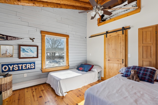 bedroom with ceiling fan, a baseboard heating unit, beam ceiling, a barn door, and light wood-type flooring