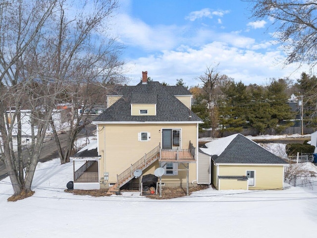 snow covered back of property with a chimney, stairs, and roof with shingles