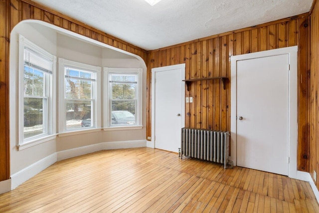 empty room featuring a wealth of natural light, light wood-style flooring, and radiator heating unit