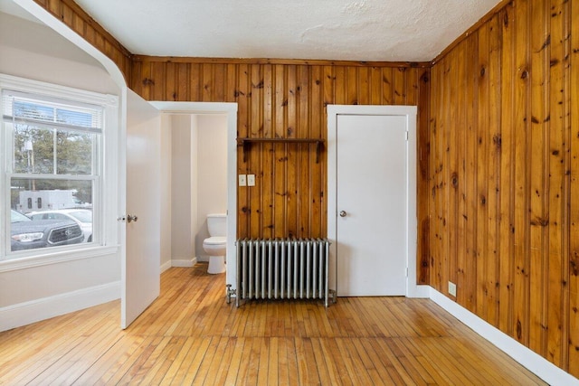 empty room with light wood finished floors, wood walls, and radiator