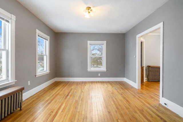 spare room with radiator heating unit, baseboards, and light wood-type flooring