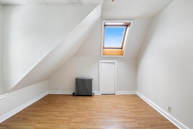 additional living space with lofted ceiling, radiator heating unit, baseboards, and light wood-type flooring