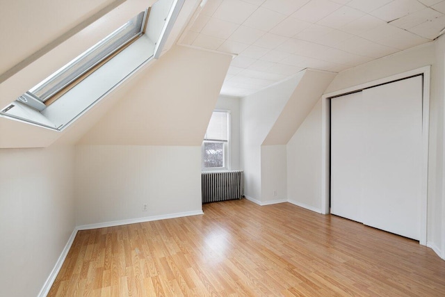 bonus room featuring baseboards, vaulted ceiling with skylight, wood finished floors, and radiator heating unit