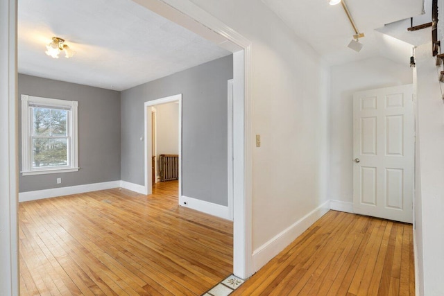 corridor with baseboards, radiator heating unit, and light wood finished floors