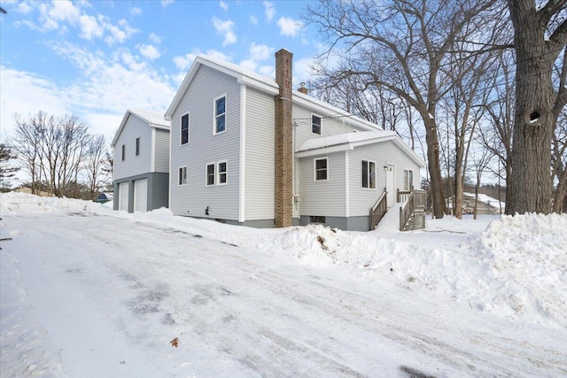 view of snowy exterior featuring a chimney and an attached garage