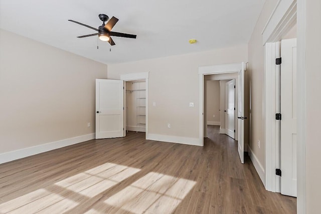 unfurnished bedroom with ceiling fan, a walk in closet, and wood-type flooring