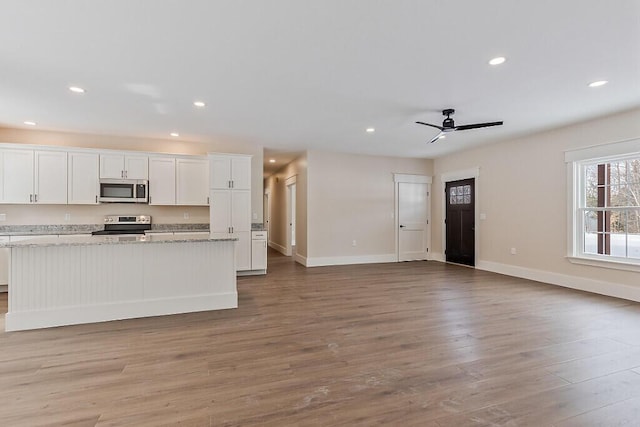 kitchen featuring light hardwood / wood-style flooring, stainless steel appliances, light stone counters, white cabinets, and ceiling fan