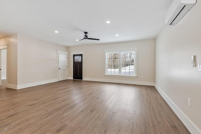 unfurnished living room featuring a wall mounted air conditioner, ceiling fan, and light hardwood / wood-style flooring