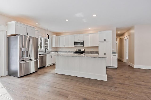 kitchen with hanging light fixtures, stainless steel appliances, light stone counters, white cabinets, and a kitchen island