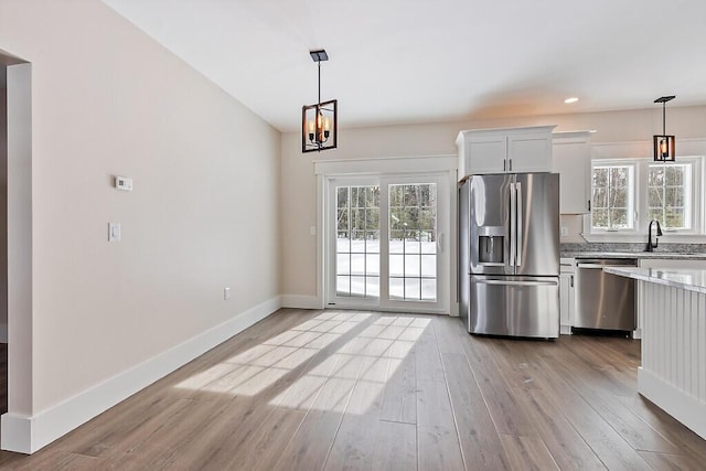 kitchen featuring light wood-type flooring, white cabinetry, decorative light fixtures, sink, and appliances with stainless steel finishes