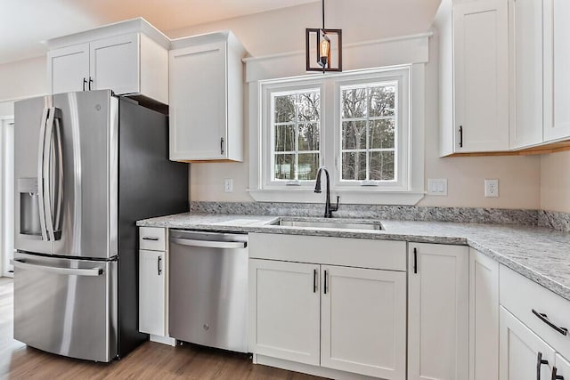 kitchen with stainless steel appliances, sink, light stone counters, white cabinets, and pendant lighting