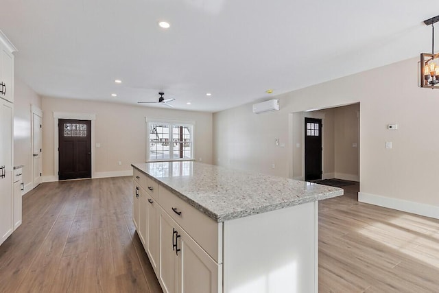 kitchen featuring white cabinets, light stone countertops, a center island, and pendant lighting