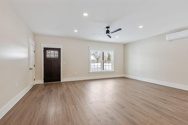 entrance foyer with ceiling fan, a wall unit AC, and light hardwood / wood-style floors