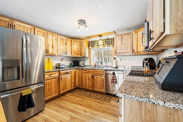 kitchen featuring stainless steel appliances, light hardwood / wood-style flooring, light stone countertops, sink, and a textured ceiling