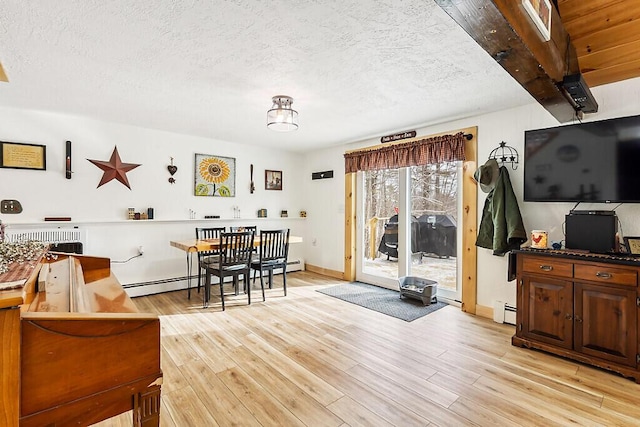 living room featuring a textured ceiling, beamed ceiling, light hardwood / wood-style floors, and a baseboard heating unit