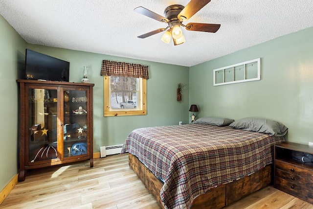 bedroom with light hardwood / wood-style floors, ceiling fan, a baseboard heating unit, and a textured ceiling