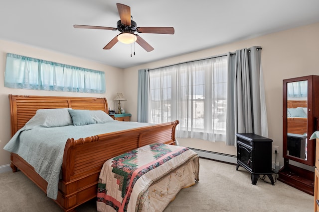 carpeted bedroom featuring a baseboard radiator, a wood stove, and ceiling fan