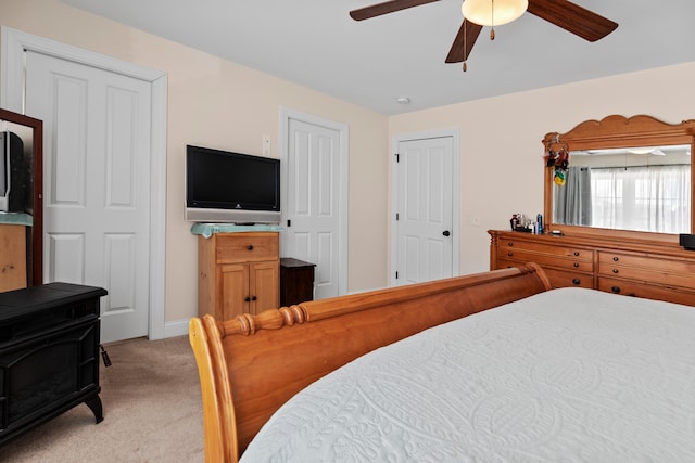 bedroom featuring light carpet, a wood stove, and ceiling fan