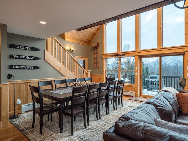 dining area featuring high vaulted ceiling, hardwood / wood-style floors, wooden walls, and baseboard heating