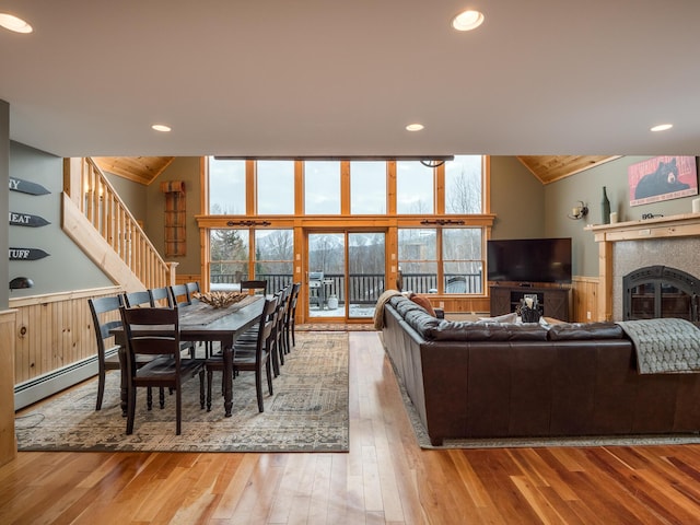 living room with vaulted ceiling, floor to ceiling windows, light wood-type flooring, a baseboard heating unit, and a tiled fireplace