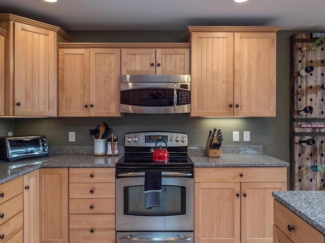 kitchen with stainless steel appliances, dark stone counters, and light brown cabinetry