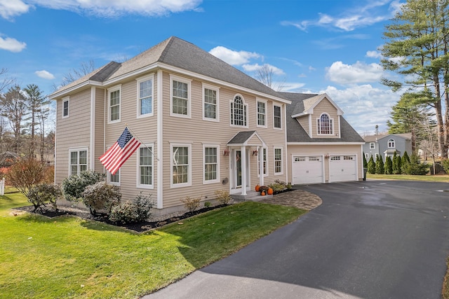 colonial house with a garage, roof with shingles, driveway, and a front lawn