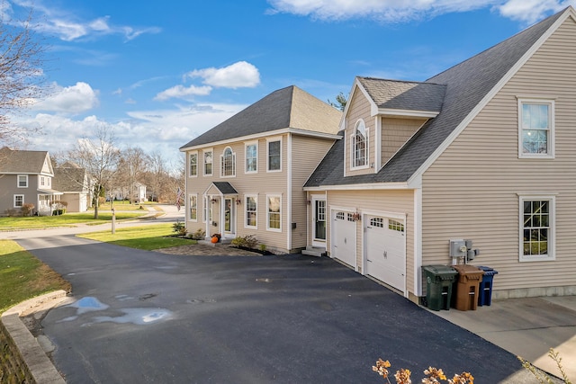 view of property exterior featuring an attached garage, a shingled roof, a residential view, and aphalt driveway