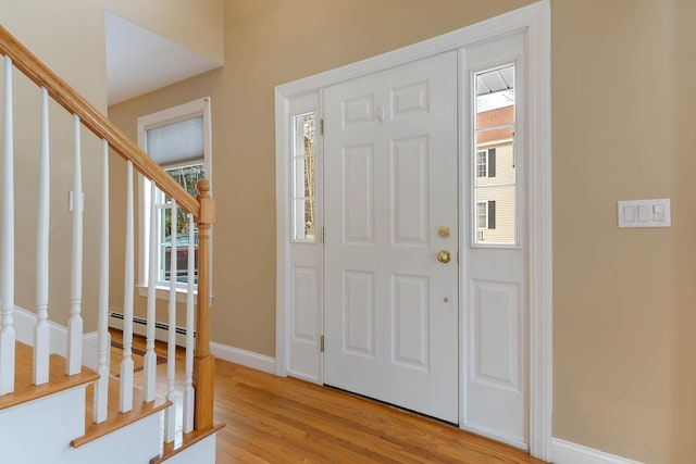 entrance foyer with a baseboard heating unit, light wood-type flooring, a healthy amount of sunlight, and stairway