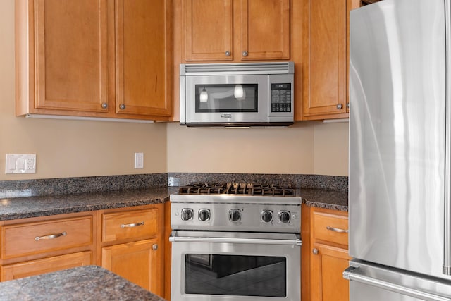 kitchen with dark stone counters, stainless steel appliances, and brown cabinets