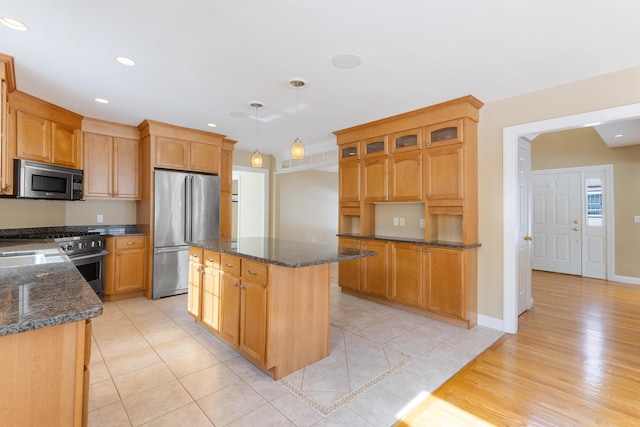 kitchen featuring premium appliances, hanging light fixtures, glass insert cabinets, a kitchen island, and dark stone countertops