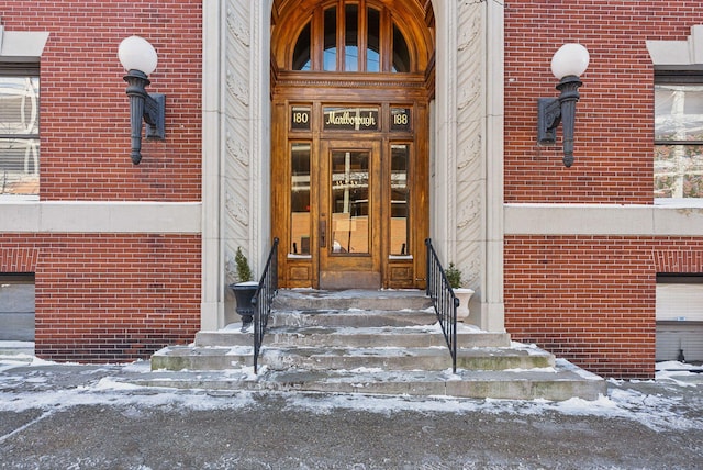 snow covered property entrance featuring brick siding