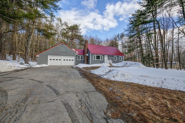 view of front of property with a garage, metal roof, aphalt driveway, and a chimney