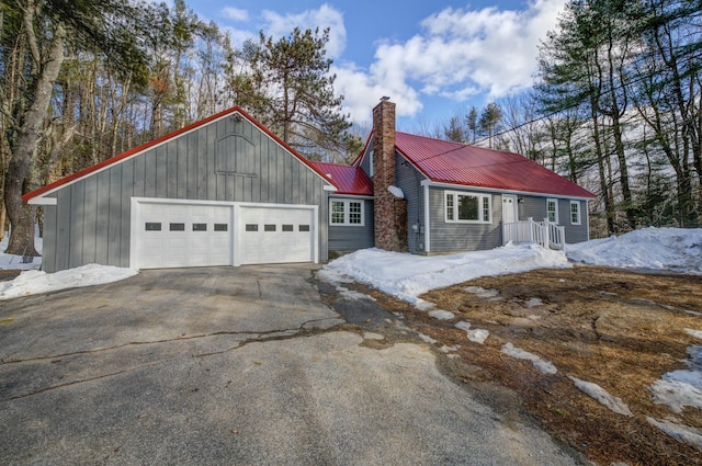 view of front of home featuring aphalt driveway, metal roof, a chimney, and a garage