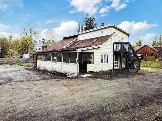 rear view of property with roof with shingles, a deck, stairway, and a sunroom
