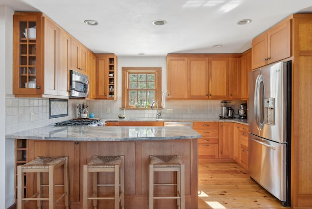 kitchen featuring light stone counters, a breakfast bar area, a peninsula, appliances with stainless steel finishes, and glass insert cabinets