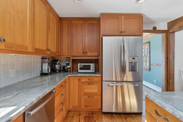 kitchen featuring light stone counters, light wood-style flooring, a toaster, stainless steel appliances, and decorative backsplash