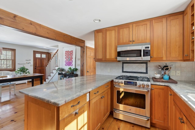 kitchen featuring decorative backsplash, light stone counters, brown cabinets, a peninsula, and stainless steel appliances