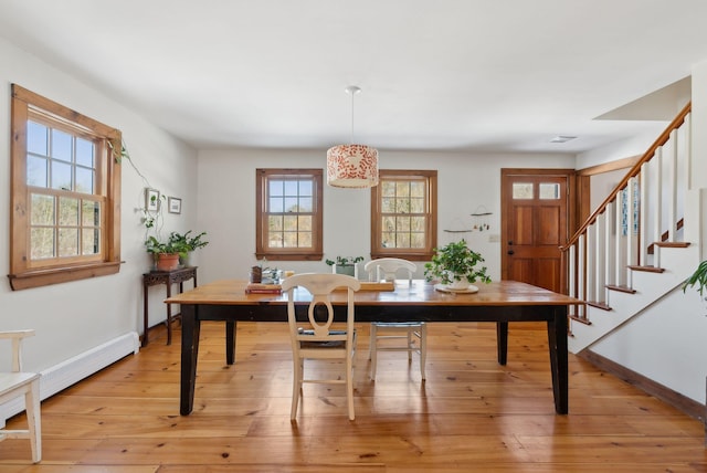 dining room featuring light wood-style floors, a baseboard heating unit, stairway, and baseboards