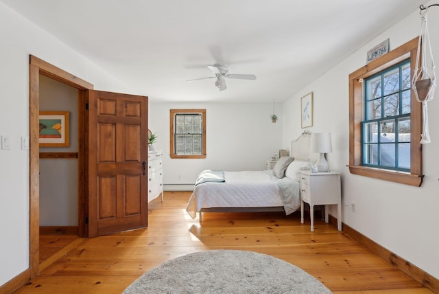 bedroom featuring ceiling fan, light wood finished floors, baseboard heating, and baseboards