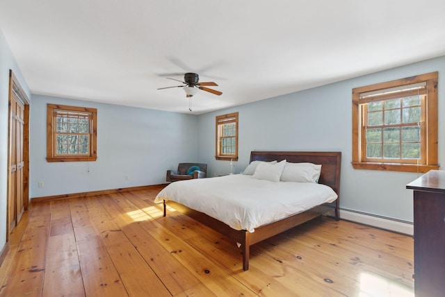 bedroom featuring a baseboard heating unit, light wood finished floors, and multiple windows