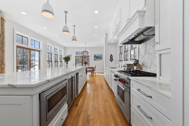 kitchen featuring white cabinets, custom range hood, pendant lighting, and stainless steel appliances