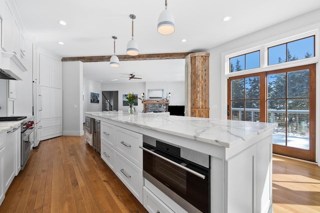 kitchen featuring white cabinets, appliances with stainless steel finishes, open floor plan, light stone countertops, and pendant lighting