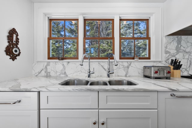 kitchen featuring light stone counters, a wealth of natural light, white cabinetry, and a sink